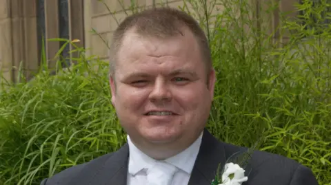 Handout PC Neil Doyle, who has short light brown hair, smiles at the camera while wearing a grey wedding suit with a white flower attached to the lapel