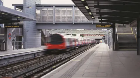 Platform at Stratford station shows departing Jubilee line train on left with bridge ahead and steps to the right. A departure board shows Waterloo