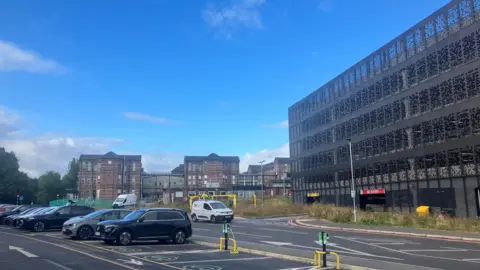 North Manchester General Hospital, including the new multi-storey car park. The image shows the Victorian Hospital in the background and a surface car park in the foreground.
