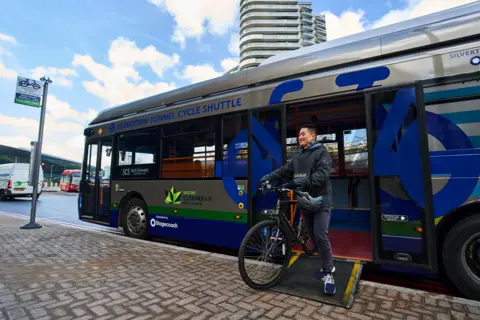 TfL Man with bike uses ramp to disembark bus which says Silvertown Tunnel Cycle Shuttle