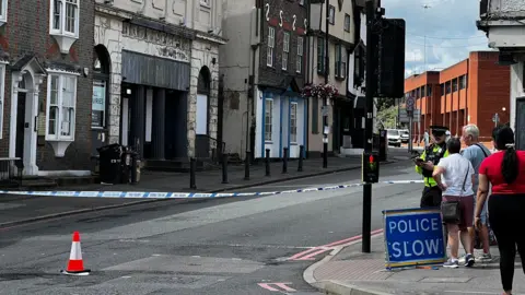 A picture of a police cordon at the bottom of Castle Street in Reading, with a police officer talking to a couple and a woman watching on.