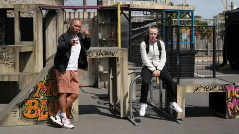 Two people sitting in a park. They are sitting on the apparatus and there is graffiti in the park. 