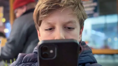 Getty Images A 12-year-old boy looks at a iPhone screen on January 26, 2024 