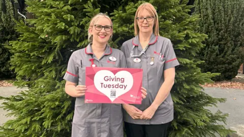 Myton Hospices Two nurses holding a card that says giving Tuesday on it