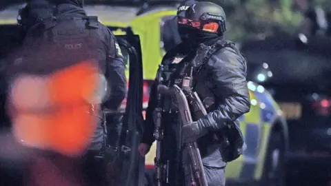 PA Media An armed police officer holds a breaching shotgun