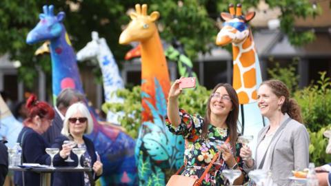 Two women taking a selfie in front of several colourful giraffe sculptures