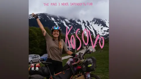 Matilda Pine Matilda Pine stands next to her bike and has an arm raised. She is near mountains in Kosovo. She has written on her photo "Kosovo, the place I never intended to find".