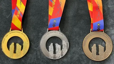 Gold, silver and bronze medals with the shape of three standing stones cut out in a circular piece of metal, on colourful ribbons.