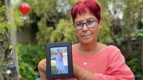 Claire Adkins' mother Julia Earlam holding a picture of her in a garden. 