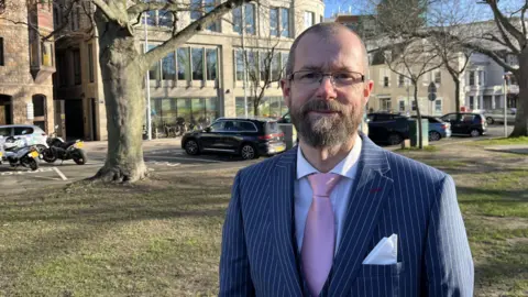 Man in pinstripe suit standing in front of states building on grass