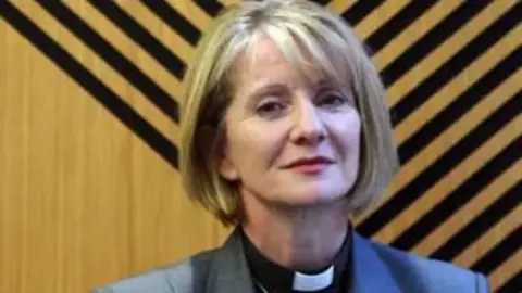 Bishop of Warrington in front of wooden wall with black stripes