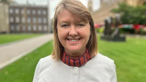 Sarah Gibson smiling at the camera in front of the Houses of Parliament in Westminster