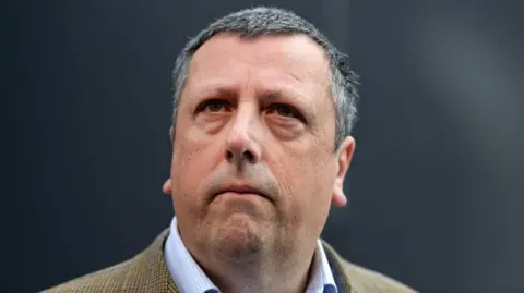 Getty Images A head shot of David Campbell who has short grey hair and is wearing a beige checked blazer and a light blue shirt. 


