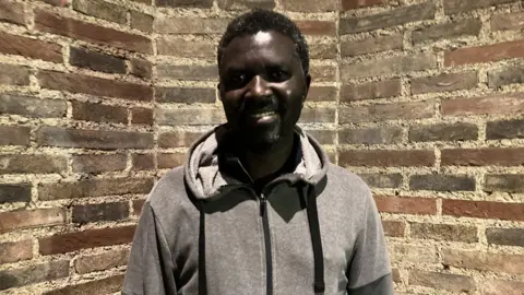 BBC Barton House resident Yousif Ahmed looking at the camera with a wall behind him