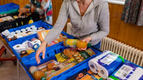 A volunteer sorts food and household supplies into crates at a food bank