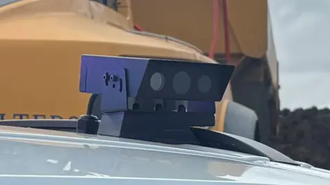 Cambridgeshire Police An ANPR camera on top of a police car. It is a rectangular box with three lenses at the front. 