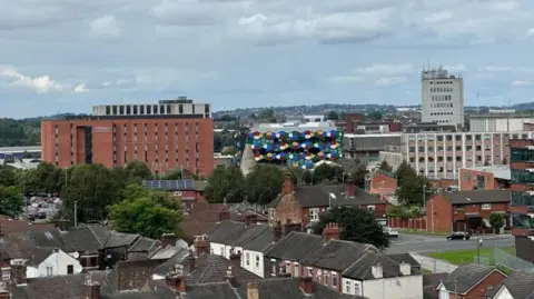 Elevated shot of the city-scape of Stoke-on-Trent, that features terraced homes in the foreground and a series of larger buildings further afield, including Hanley's One Smithfield building.
