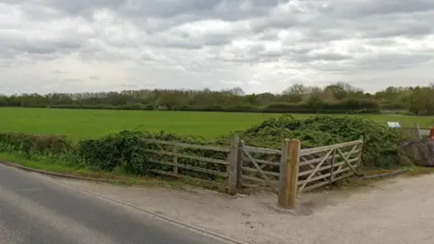 A patch of land with fields and a wooden fence and gates - next to a road in York 