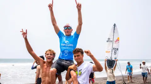 Rip ‍Curl ⁣Lukas Skinner being ⁣hoisted ​onto ‌the shoulders of two ‍other surfers after winning an event