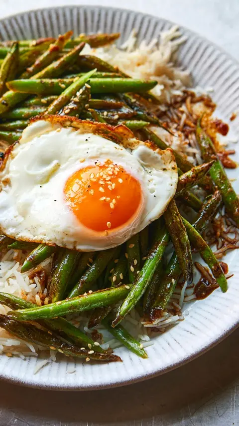Green beans and rice topped with a fried egg sit in a grey bowl