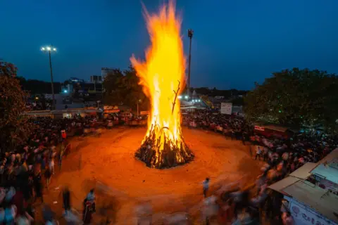 A bonfire is lit on the occasion of Getty Image Holi Festival, which consists of people around it in a circle.