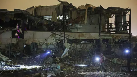 Getty Images People walking around the ruined of an exploded building at night time with torches 