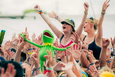 Harris Tomlinson-Spence/Truck Festival The Truck audience singing, arms aloft. Two girls are sat on shoulders. A Kermit puppet is held aloft.