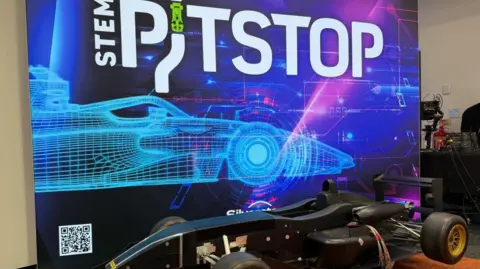 Robert Constantin/BBC A poster with "STEM PITSTOP" written on it with a blue print of an F1 car. Beneath it is a small black racing car.