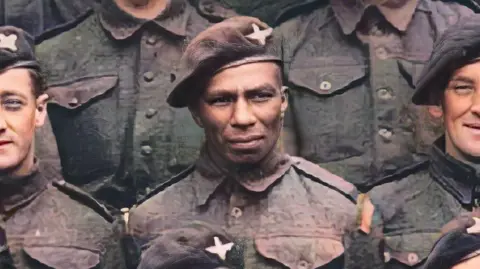 Members of the Parachute Regiment pose in uniform and berets. The original black and white picture has been colourised. Sidney Cornell is flanked by four white paratroopers in this cropped image of part of the group.