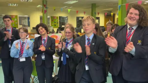 Six school pupils in uniform standing in a line clapping