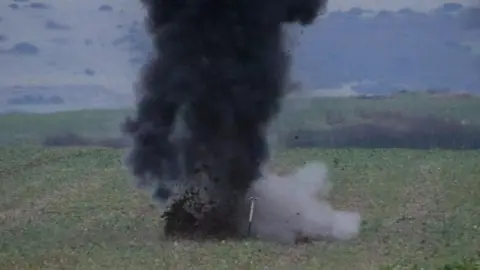 Green field with cloud of black and grey smoke as device blown up.