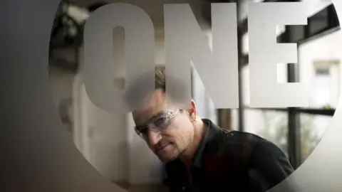 Getty Images Bono looks through a sheet of glass which is etched with the logo of his charity organisation One