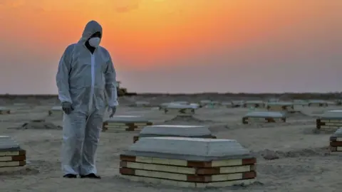 Getty Images A masked grave digger observers the graves in a cemetery in Iraq