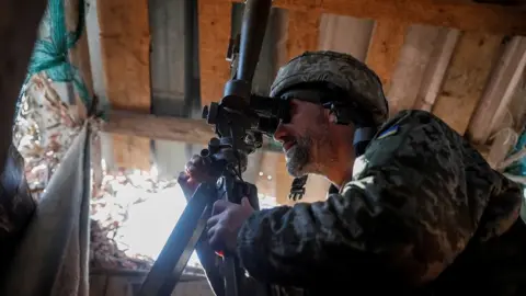 Reuters A Ukrainian service member uses a periscope while observing the area at a position on the front line near the village of Travneve in Donetsk region