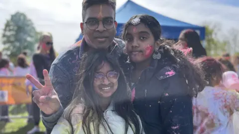 Jon Wright/BBC Sri Tedla with his two daughters covered in the coloured powder