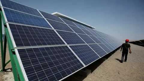 Getty Images A Chinese worker walks between solar panels in Dunhuang, in China's northwest Gansu Province