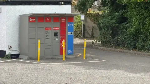 A locker for parcels is pictured in a car park.