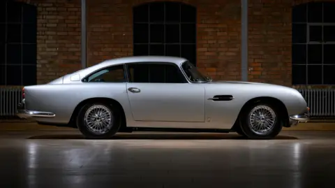 Dominic Fraser/Aston Martin Works The fully restored car with gleaming silver paint stands on the floor of a showroom