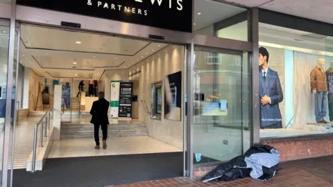 Someone sleeps in a sleeping bag at the entrance to a John Lewis.