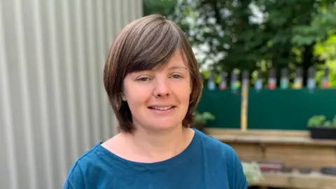 A woman with short brown hair looking at the camera. She has a blue t-shirt on