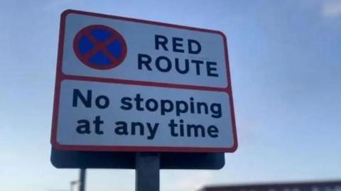 A red route sign notifying drivers that they must not stop at any time