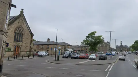 A car park in Buxton town centre with a road to the right and a church to the left.