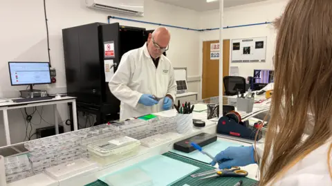 BBC/Richard Moss A man in a white lab coat works at a table in a lab setting.