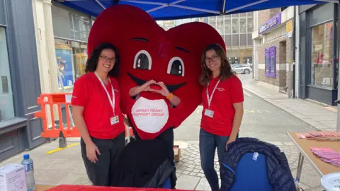 Two women in red polo shirts and a big red heart mascot