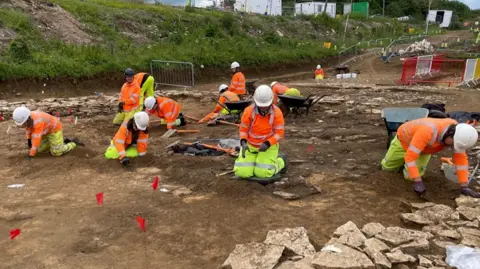 A group of archaeologists wearing protective gear, working on the A417 excavation.