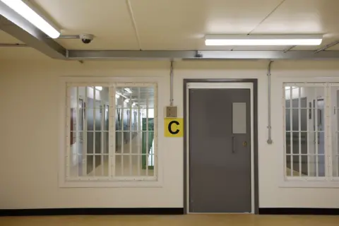 Getty Images A cell block can be seen with the letter 'C' hanging by the door. Through windows either side of the door a corridor with a row of more doors can be seen.