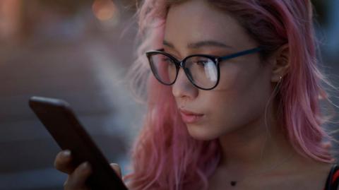 A stock image of a young woman with pink hair looking at a smart phone