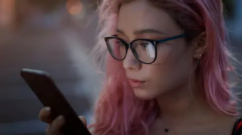 Getty Images A stock image of a young woman with pink hair looking at a smart phone