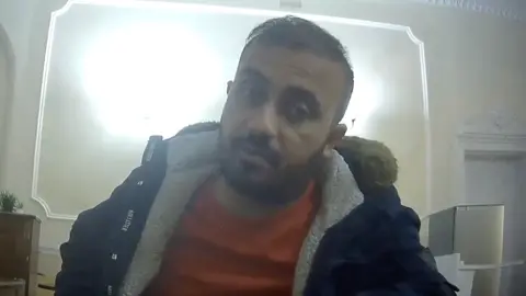 Zahid Hasan Akhand, a bearded man wearing a fleece jacket and jumper and sitting at a desk, in a picture taken by an undercover reporter