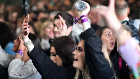 Getty Images A young pistillate  clubber points her telephone  towards the stage, surrounded by different   clubbers